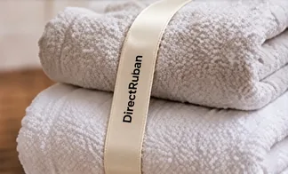 Serviettes éponge blanches pliées, tenues par un ruban satin crème imprimé DirectRuban en noir